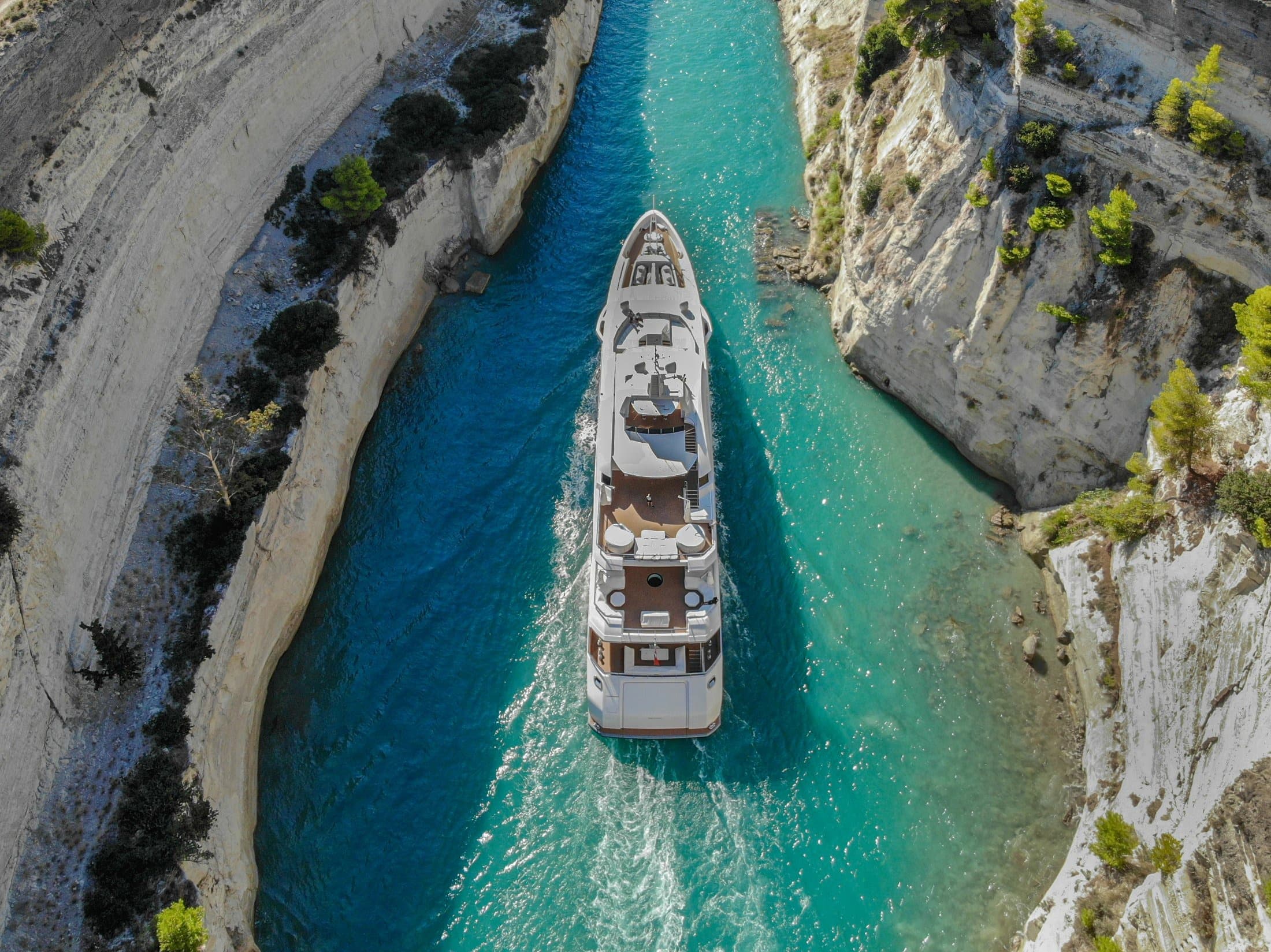 A superyacht seen from directly above, under way through the narrow limestone walls of the Corinth Canal