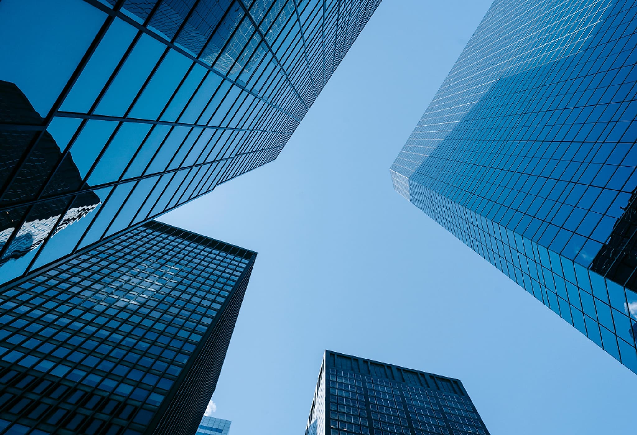 Glass office towers seen from street level, converging against a clear sky